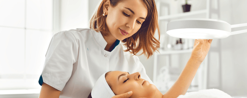 A dermatologist examining a patient's face under a clinical lamp during a minor skin procedure consultation in Sydney